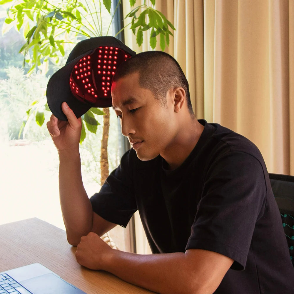 Person wearing a black cap with red LED lights on a desk indoors